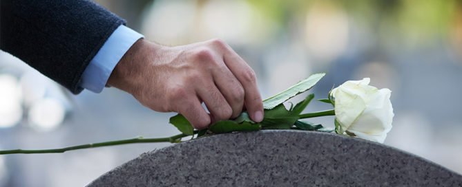An image of a man putting a white rose on a memorial to pay his respects.