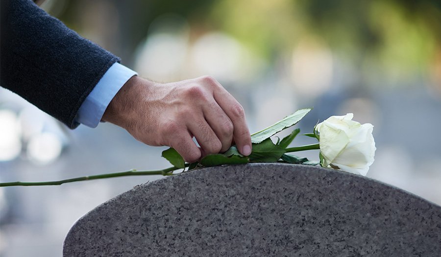 An image of a man putting a white rose on a memorial to pay his respects.