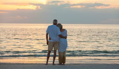 An image of a grieving couple on the beach looking at the sunset,.